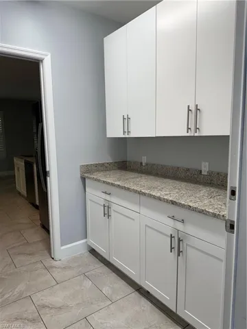 Kitchen with light stone countertops, refrigerator, white cabinetry, and dishwashing machine