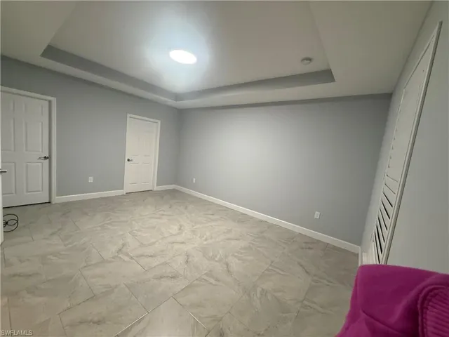 Bedroom with marble finish floor, a tray ceiling, and baseboards