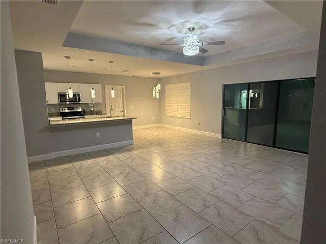 Unfurnished living room with ceiling fan with notable chandelier, sink, and a tray ceiling