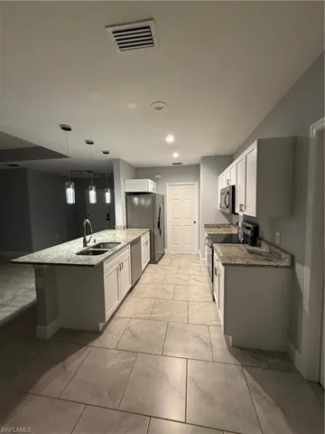 Kitchen featuring range, sink, decorative light fixtures, white cabinetry, and dishwashing machine
