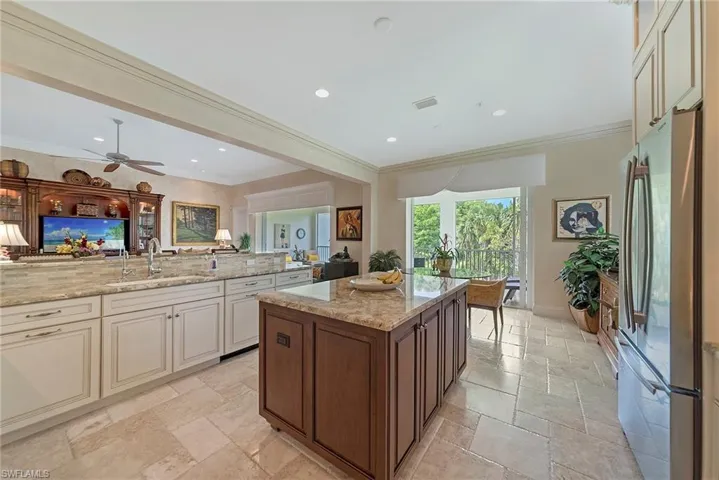 Kitchen featuring light stone countertops, freestanding refrigerator, stone tile floors, open floor plan, and crown molding