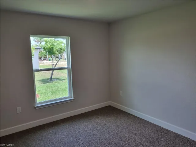 Empty room with baseboards and dark carpet