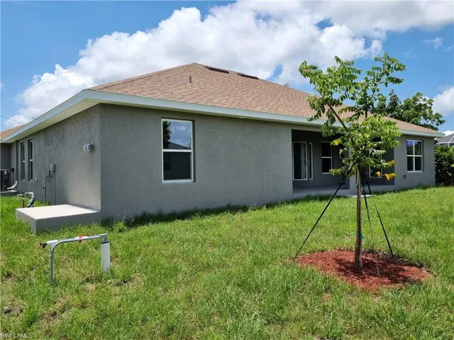 Rear view of property with stucco siding, a yard, and roof with shingles