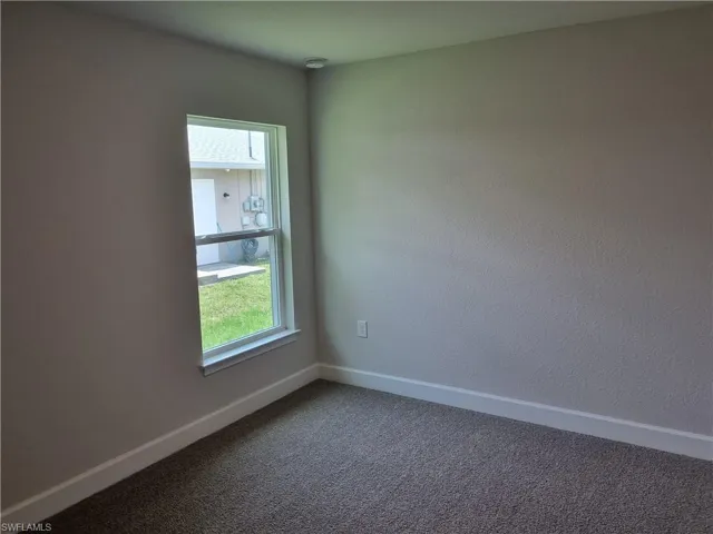 Empty room with dark colored carpet, baseboards, and a smoke detector