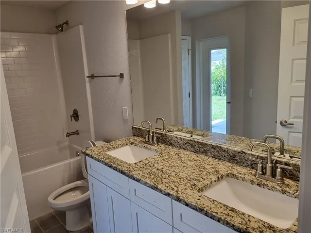 Bathroom featuring toilet, double vanity, tub / shower combination, and a textured wall