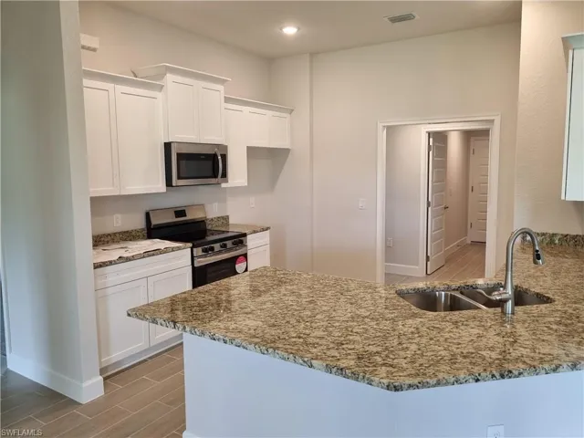Kitchen with appliances with stainless steel finishes, a sink, stone counters, white cabinets, and recessed lighting