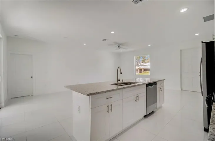 Kitchen featuring stainless steel appliances, ceiling fan, white cabinetry, an island with sink, and sink
