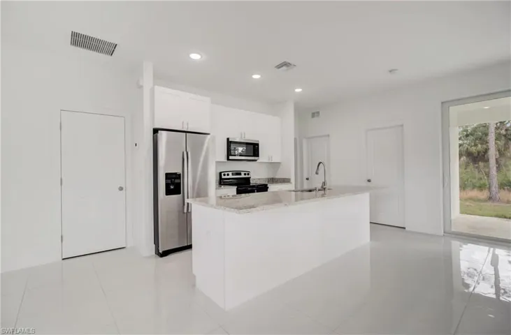 Kitchen with stainless steel appliances, white cabinetry, an island with sink, and light tile flooring