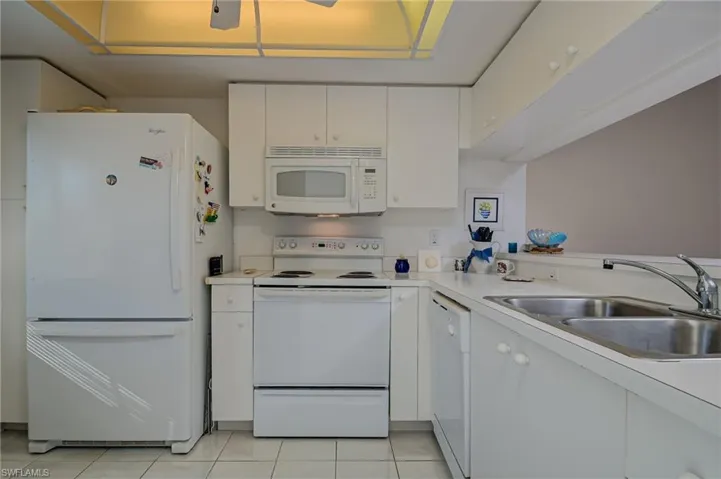 Kitchen featuring light tile patterned floors, sink, white appliances, and white cabinets