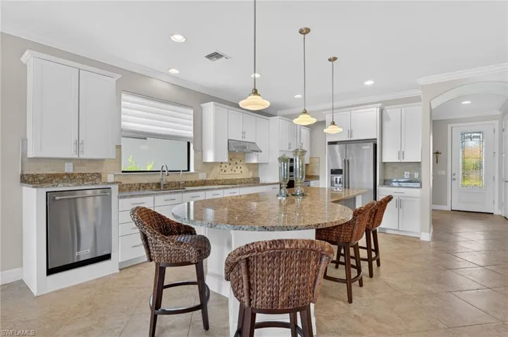 Kitchen featuring crown molding, backsplash, white cabinets, light stone countertops, and a breakfast bar area