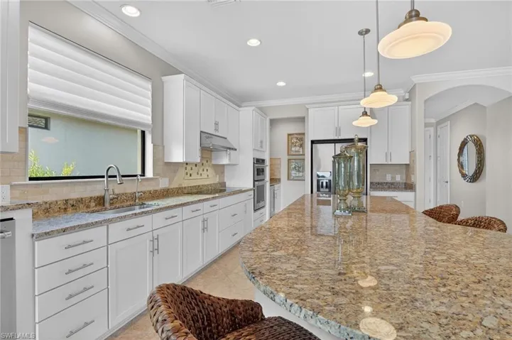 Kitchen featuring a kitchen breakfast bar, light stone countertops, ornamental molding, white cabinets, and arched walkways
