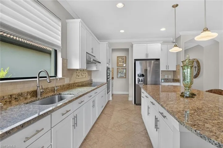 Kitchen featuring white cabinets, ornamental molding, light stone countertops, high end fridge, and hanging light fixtures