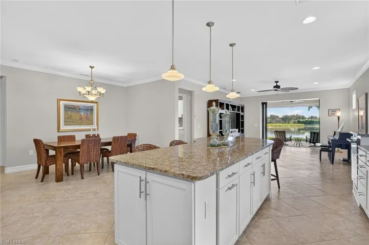 Kitchen with crown molding, a breakfast bar, white cabinetry, light stone countertops, and decorative light fixtures