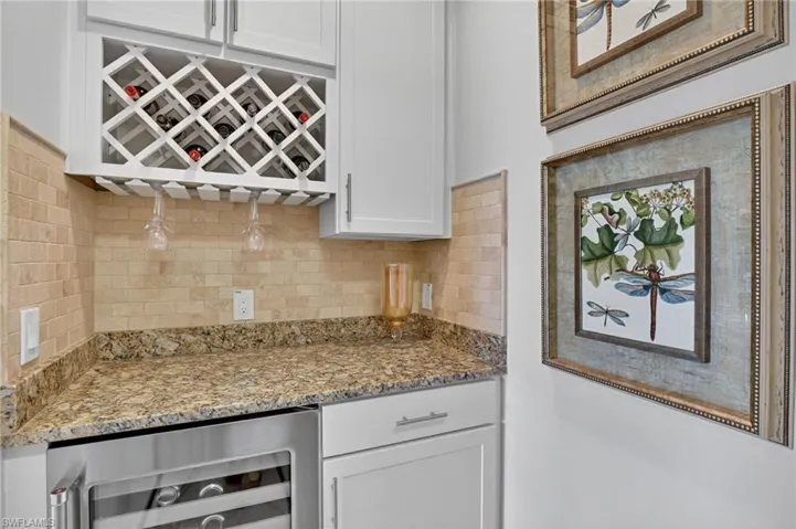 Kitchen featuring beverage cooler, white cabinetry, light stone counters, and backsplash