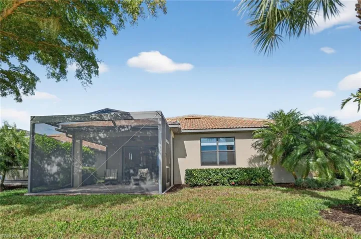 Back of house featuring a lanai, a lawn, stucco siding, and a tiled roof