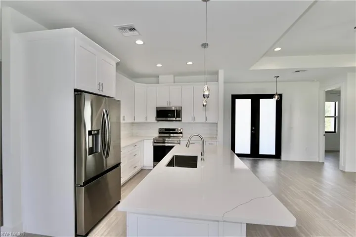 Kitchen with hanging light fixtures, stainless steel appliances, backsplash, and white cabinetry