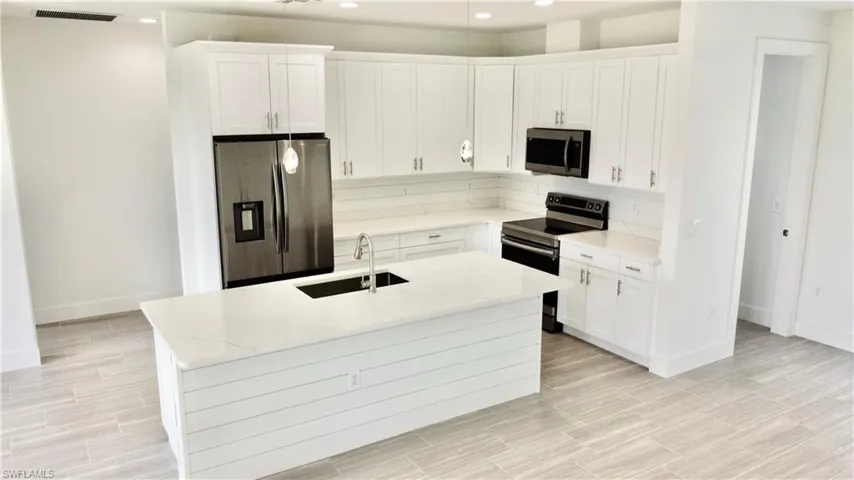Kitchen featuring appliances with stainless steel finishes, sink, tasteful backsplash, and a center island with sink
