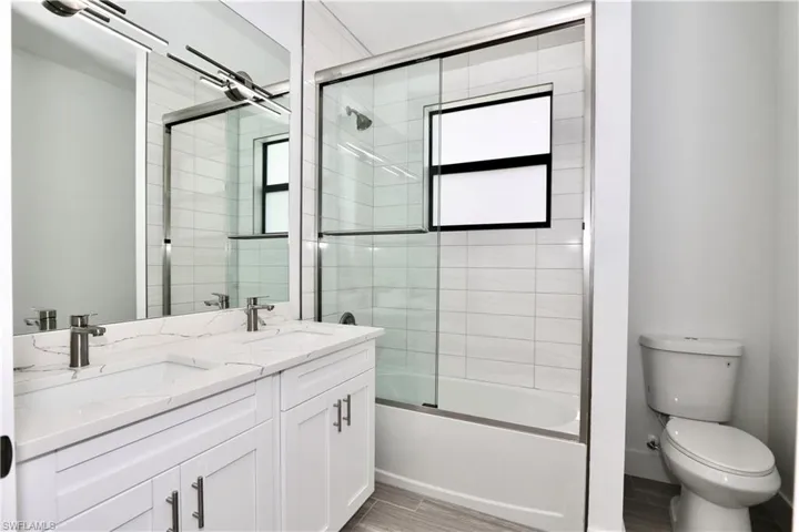 2nd bathroom featuring shower / bath combination with glass door, vanity with extensive cabinet space, and dual sinks