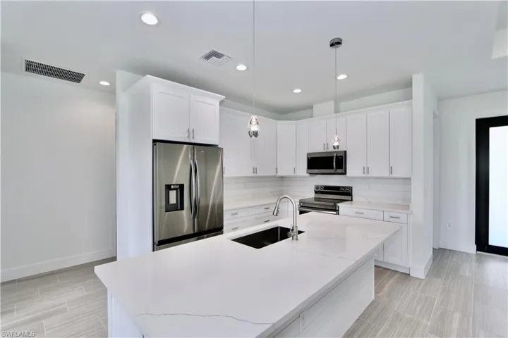 Kitchen with hanging light fixtures, a center island with sink, stainless steel appliances, white cabinets, and backsplash