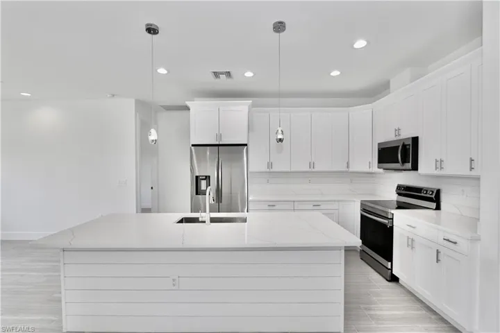 Kitchen with stainless steel appliances, a center island with sink, pendant lighting, light stone counters, and backsplash