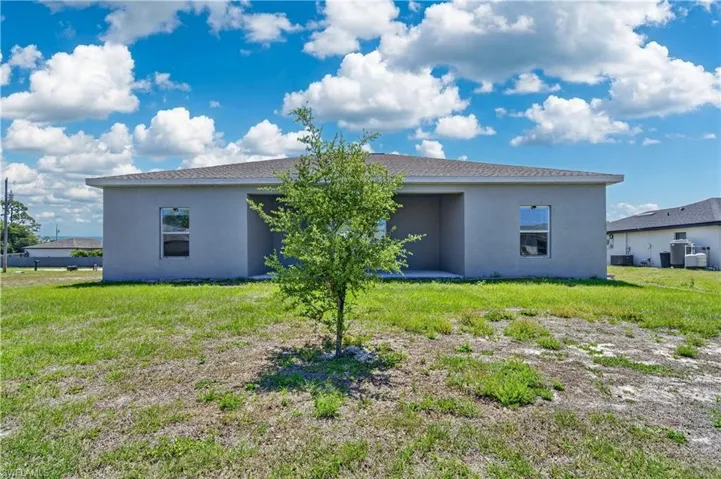 The property features a stucco exterior, a patio area, and a well-maintained lawn with a small tree
