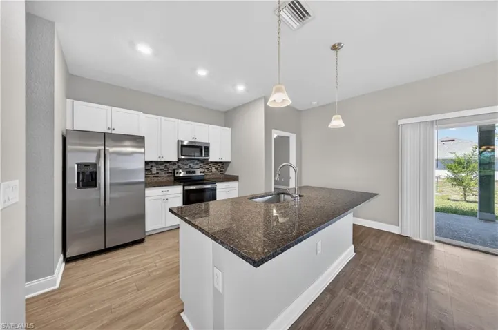 The kitchen features white cabinetry, stainless steel appliances, and an island with a sink and pendant lighting