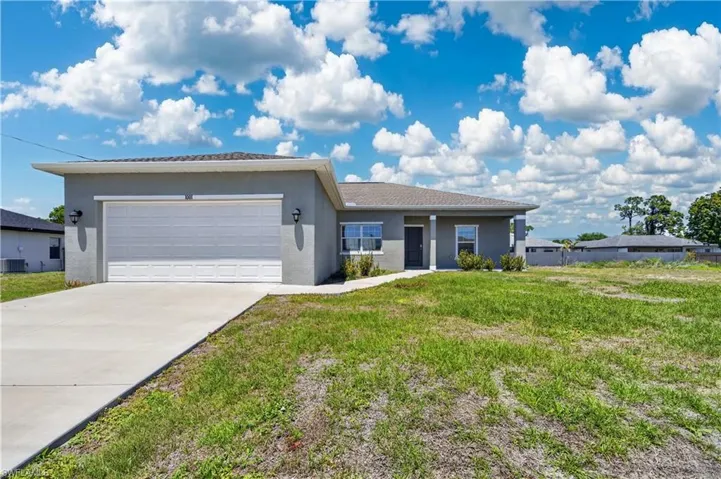 The property features a concrete driveway leading to an attached garage with a panel door, outdoor light fixtures, and a grey exterior