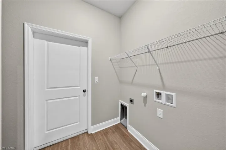 Utility room featuring wood-look flooring, a white paneled door, and a wire shelf