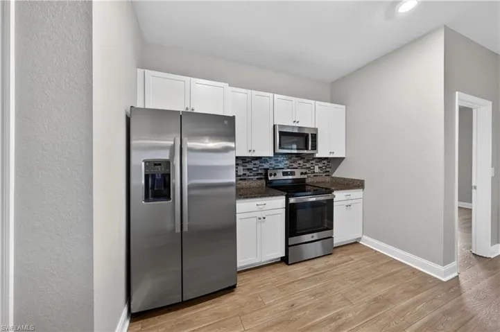 The kitchen features stainless steel appliances, white cabinetry, a tiled backsplash, and wood-look flooring