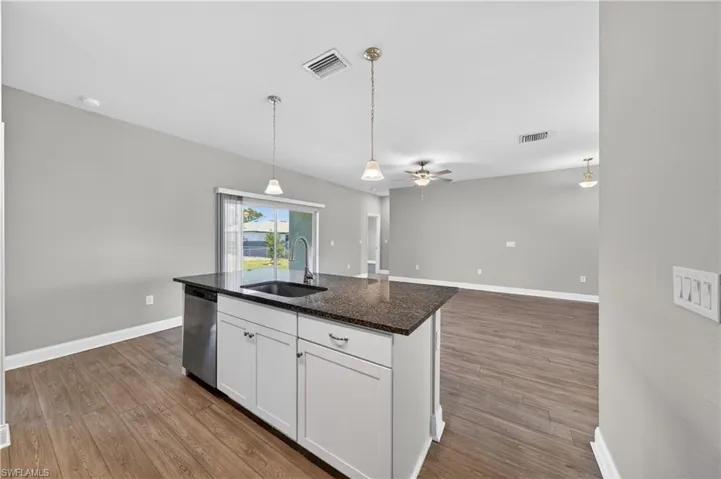 Kitchen island featuring a dark granite countertop, an undermount sink with a gooseneck faucet, and white cabinetry
