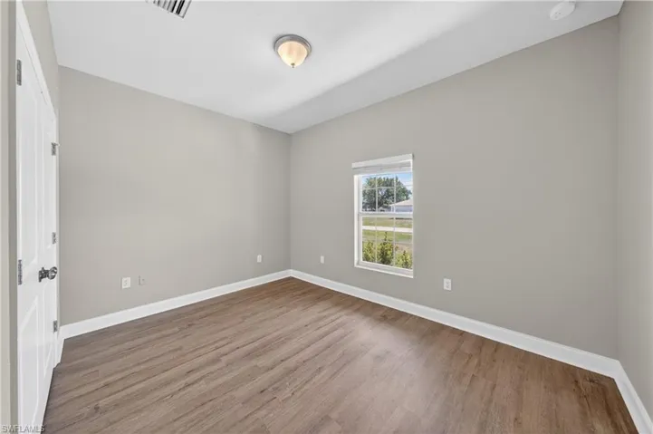 This room features durable plank flooring, light gray walls, a white ceiling, and a window providing natural light