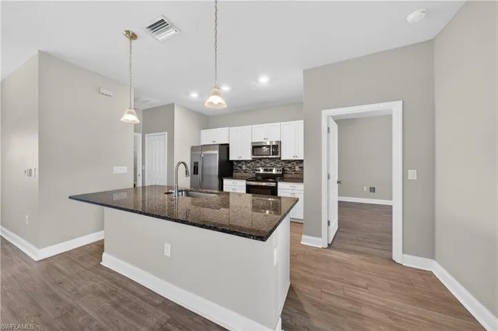 The kitchen features an island with a dark granite countertop and integrated sink, stainless steel appliances, white cabinetry, and recessed lighting