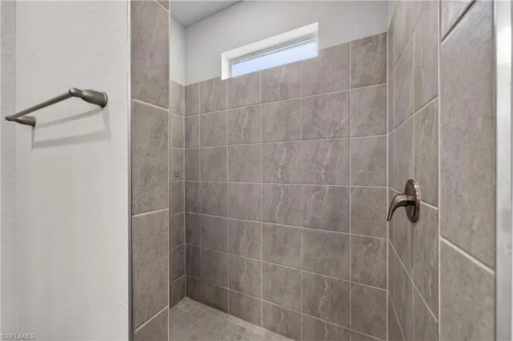 Shower featuring grey tiled walls, a window, and a bronze-toned shower fixture