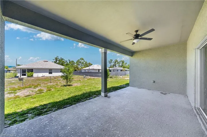 Spacious covered patio with a ceiling fan, overlooking a yard with grass and a tree