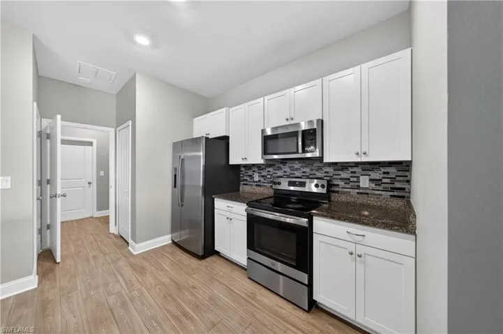 The kitchen features white cabinetry, granite countertops, a tile backsplash, and stainless steel appliances including a refrigerator, range, and microwave