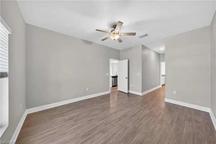 This spacious room features wood-look flooring, light gray walls, and a ceiling fan with integrated lighting