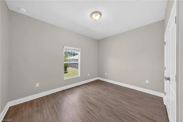 This room features wood-style flooring, a window with blinds, and a white ceiling with a flush-mount light fixture
