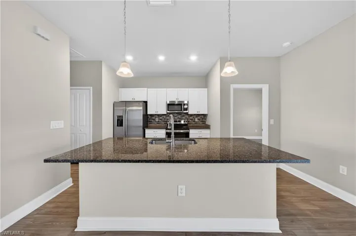 The kitchen features an island with a dark granite countertop and an integrated sink, white cabinetry, stainless steel appliances, and recessed lighting
