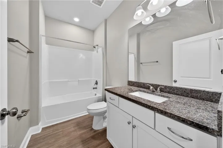 Bathroom featuring a white bathtub and shower combination, a toilet, and a vanity with a granite countertop and a rectangular sink