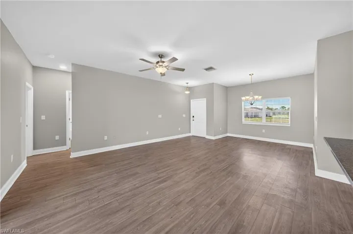 Spacious living area featuring hard surface flooring, light gray walls, a ceiling fan, and a window providing natural light