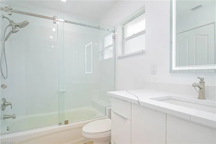 Bathroom featuring toilet, vanity, visible vents, and bath / shower combo with glass door