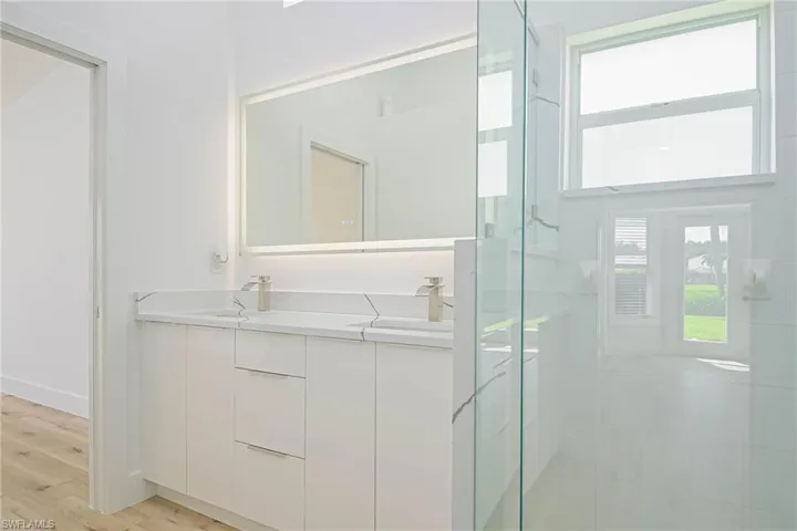 Full bath featuring a shower stall, double vanity, a sink, and wood finished floors