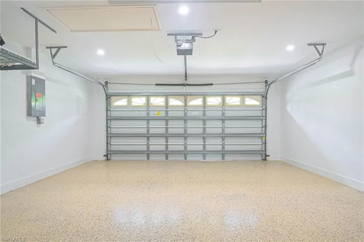Garage featuring electric panel, baseboards, and a garage door opener