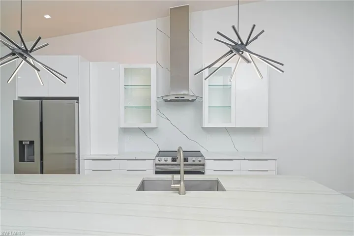 Kitchen with glass insert cabinets, white cabinets, wall chimney exhaust hood, modern cabinets, and stainless steel appliances