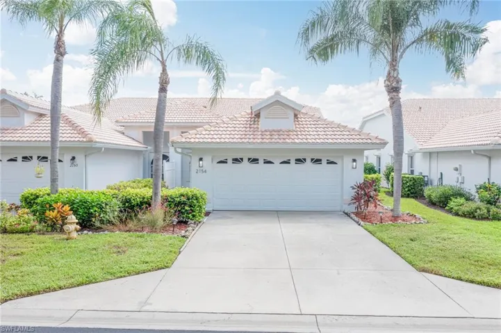 Ranch-style house with a front yard, a tile roof, driveway, and stucco siding