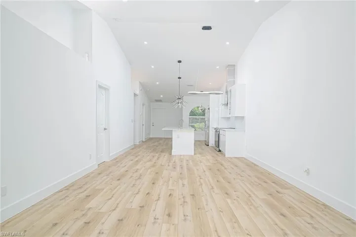 Unfurnished living room featuring a sink, light wood-style flooring, a high ceiling, and baseboards