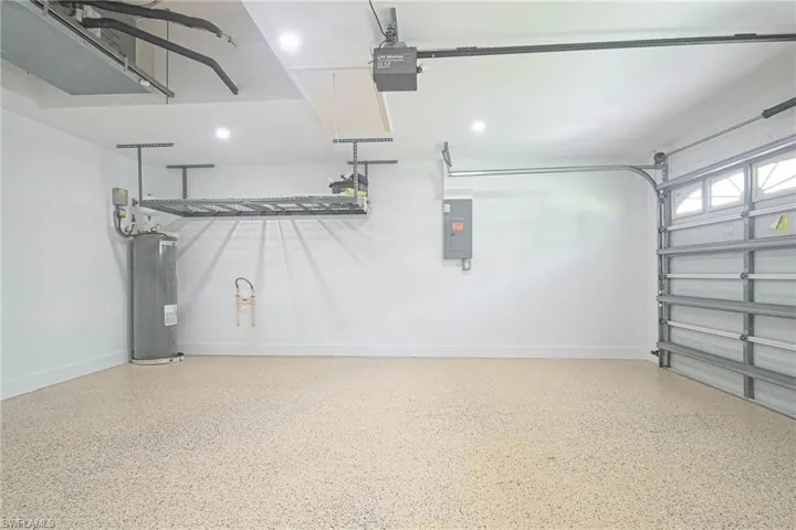 Garage featuring water heater, baseboards, a garage door opener, and electric panel