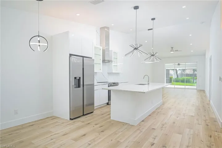 Kitchen with a notable chandelier, a sink, wall chimney range hood, white cabinetry, and stainless steel appliances