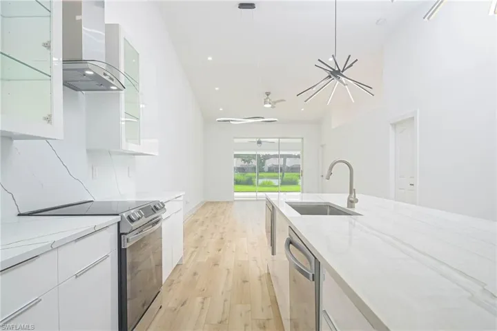 Kitchen with a sink, appliances with stainless steel finishes, wall chimney exhaust hood, and white cabinetry