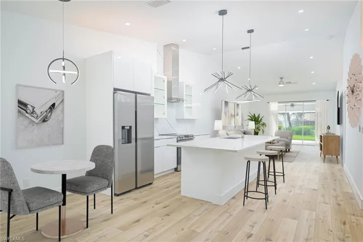 Virtually Staged Kitchen with white cabinets, modern cabinets, wall chimney range hood, light wood finished floors, and stainless steel appliances